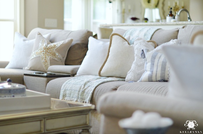 WHite and blue pillows accent a white linen couch placed in a white and  gray living room in front of a glass-paneled door f…