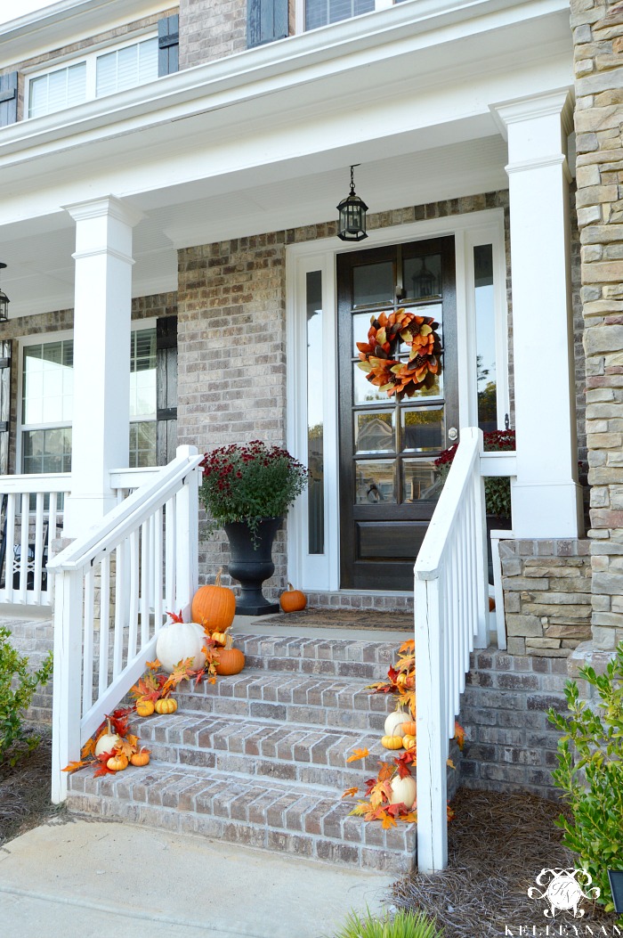 fall-porch-with-pumpkins-cascading-down-stairs-with-leaves-craftsman-style-brick-and-stone-home-with-white-columns