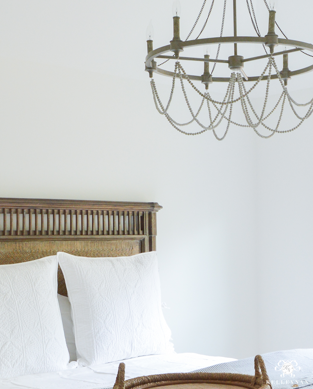 guest bedroom wooden woven cane bed with white pottery barn bedding and a chandelier