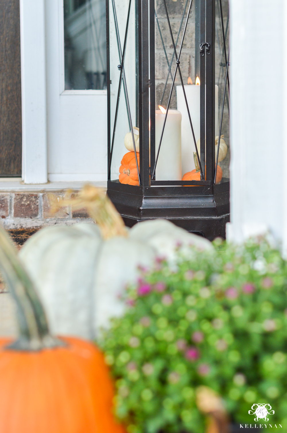 Lantern on fall front porch with candles and pumpkins