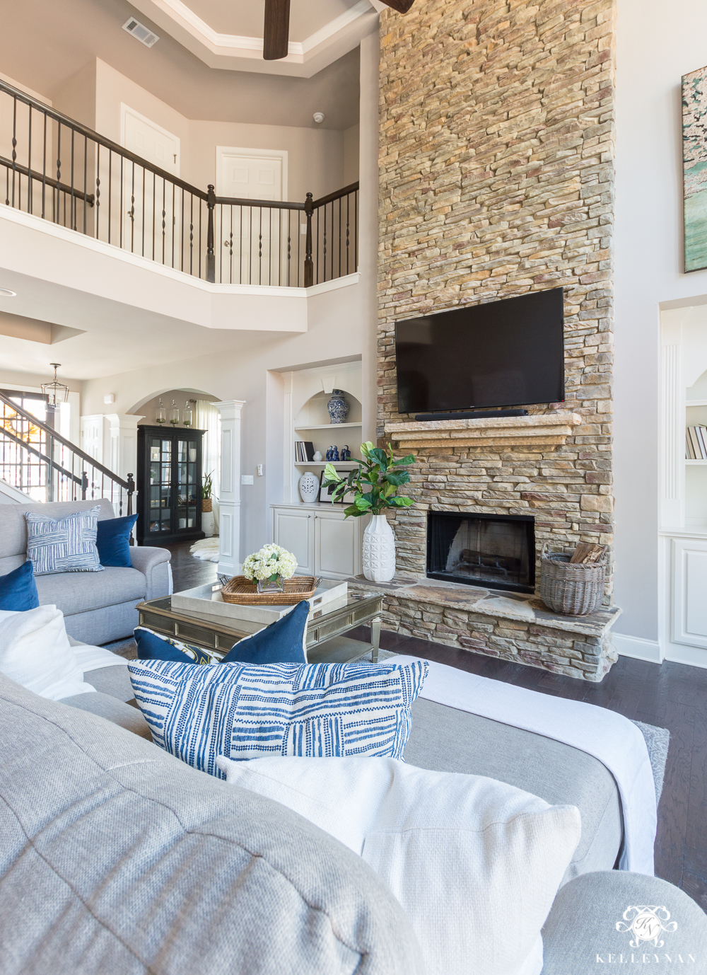 Two Story Living Room with Versatile Gray Paint and TV OVer Stacked Stone Fireplace