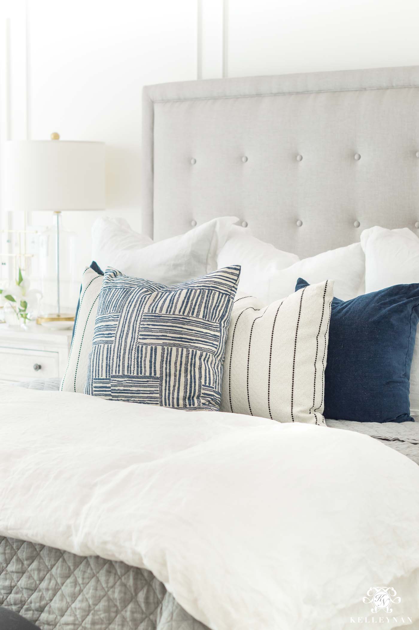 White bedding with blue and white pillows for master bedroom ideas with a tufted headboard