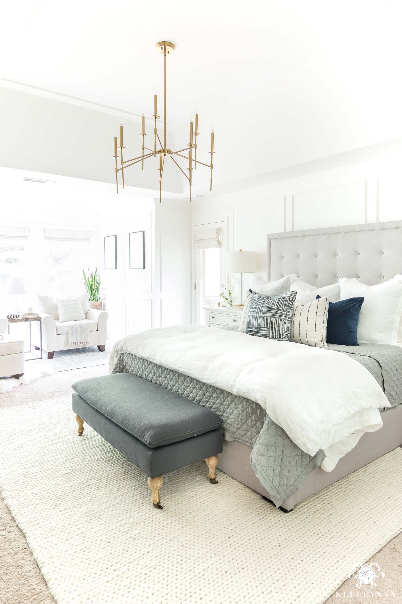 Neutral master bedroom design ideas with gray tufted headboard and brass chandelier